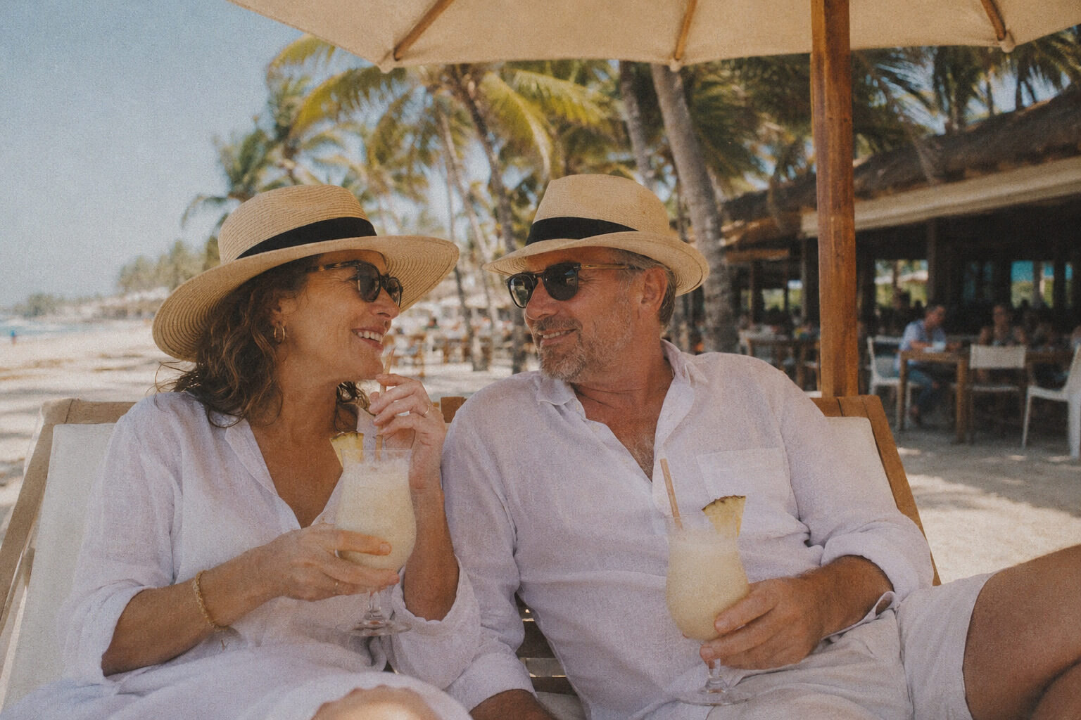 Couple enjoying their cocktails while relaxing in sunbeds close to a beach bar.